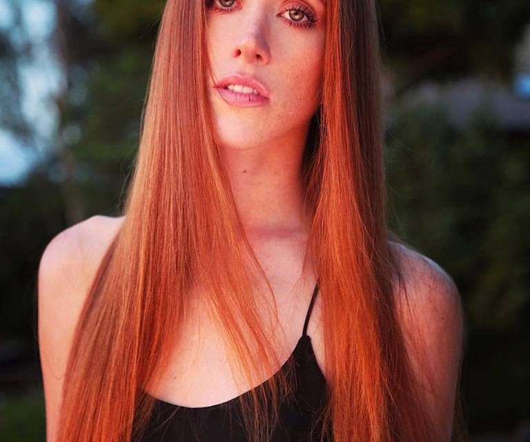 Woman with long straight red hair outdoors at sunset.